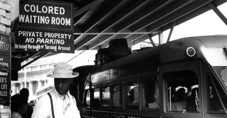 Image of African American man standing outside at a "Colored Waiting Room" at a bus stop in Durham, NC.